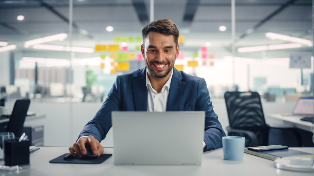 Young,Happy,Businessman,Using,Computer,In,Modern,Office,With,Colleagues.